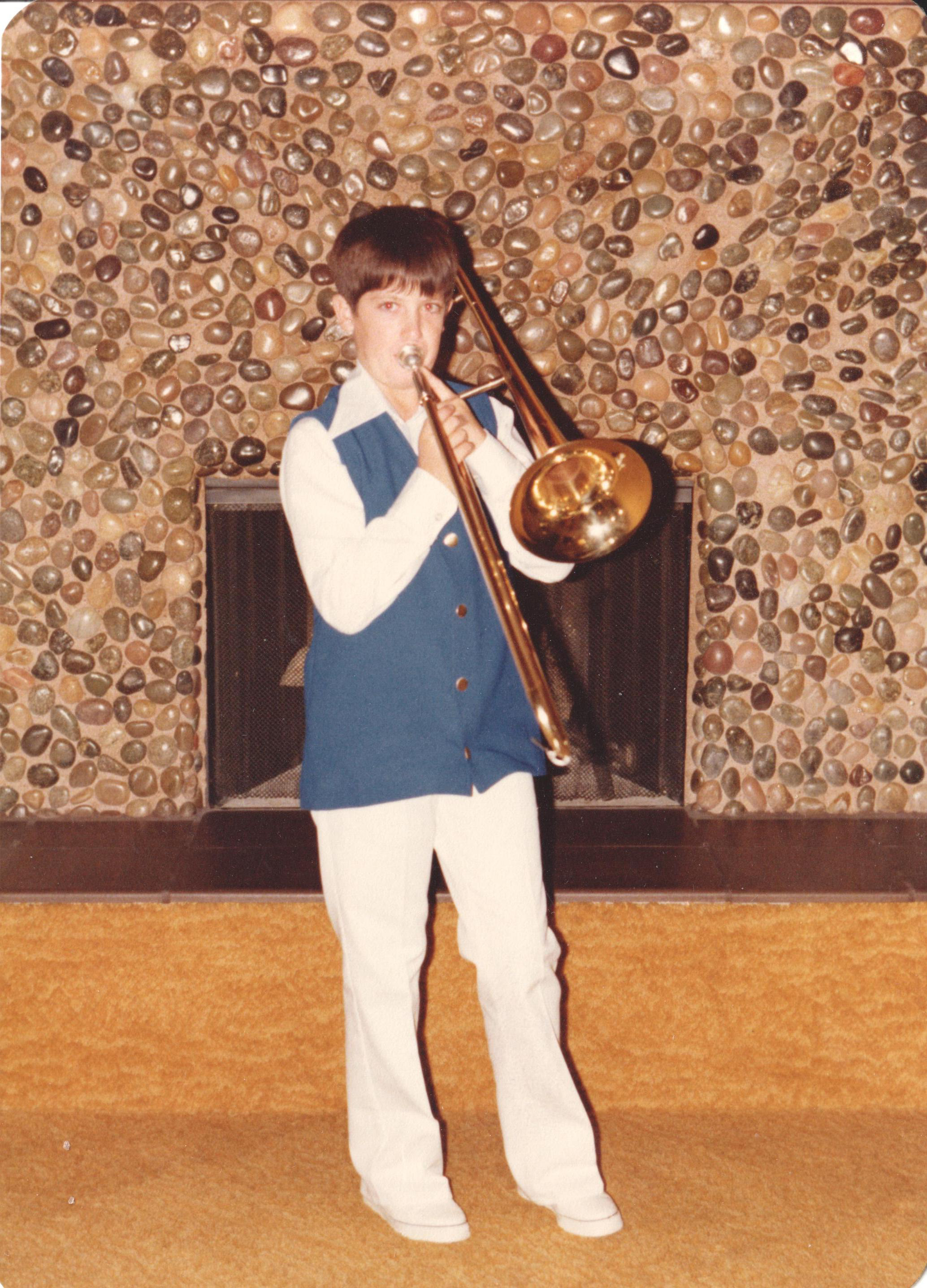 Fred (~10) playing trombone in the El Centro living room — full 1970s regalia