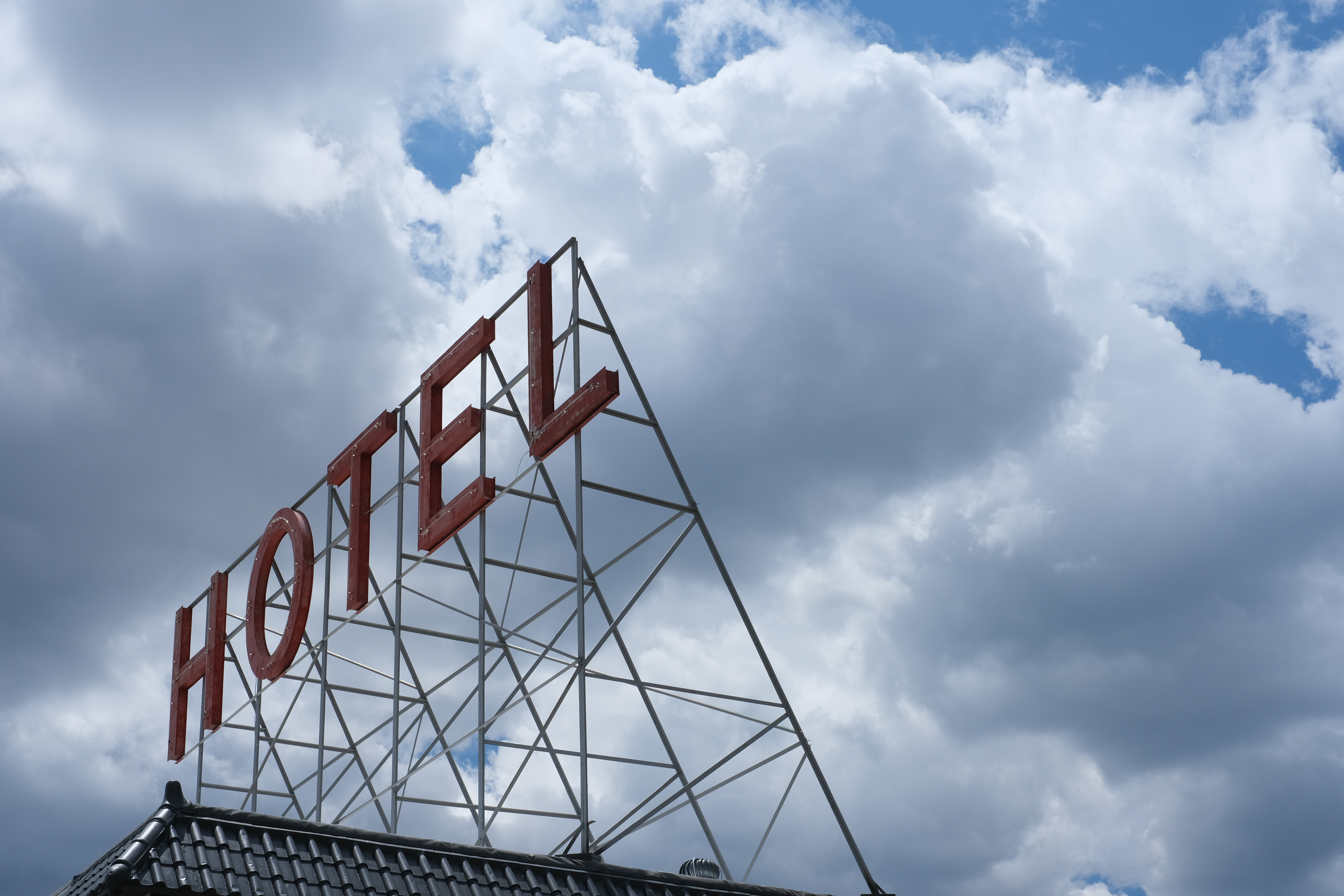 A rooftop "HOTEL" sign in red letters on a steel lattice frame, set against a dramatic sky of piled storm clouds.