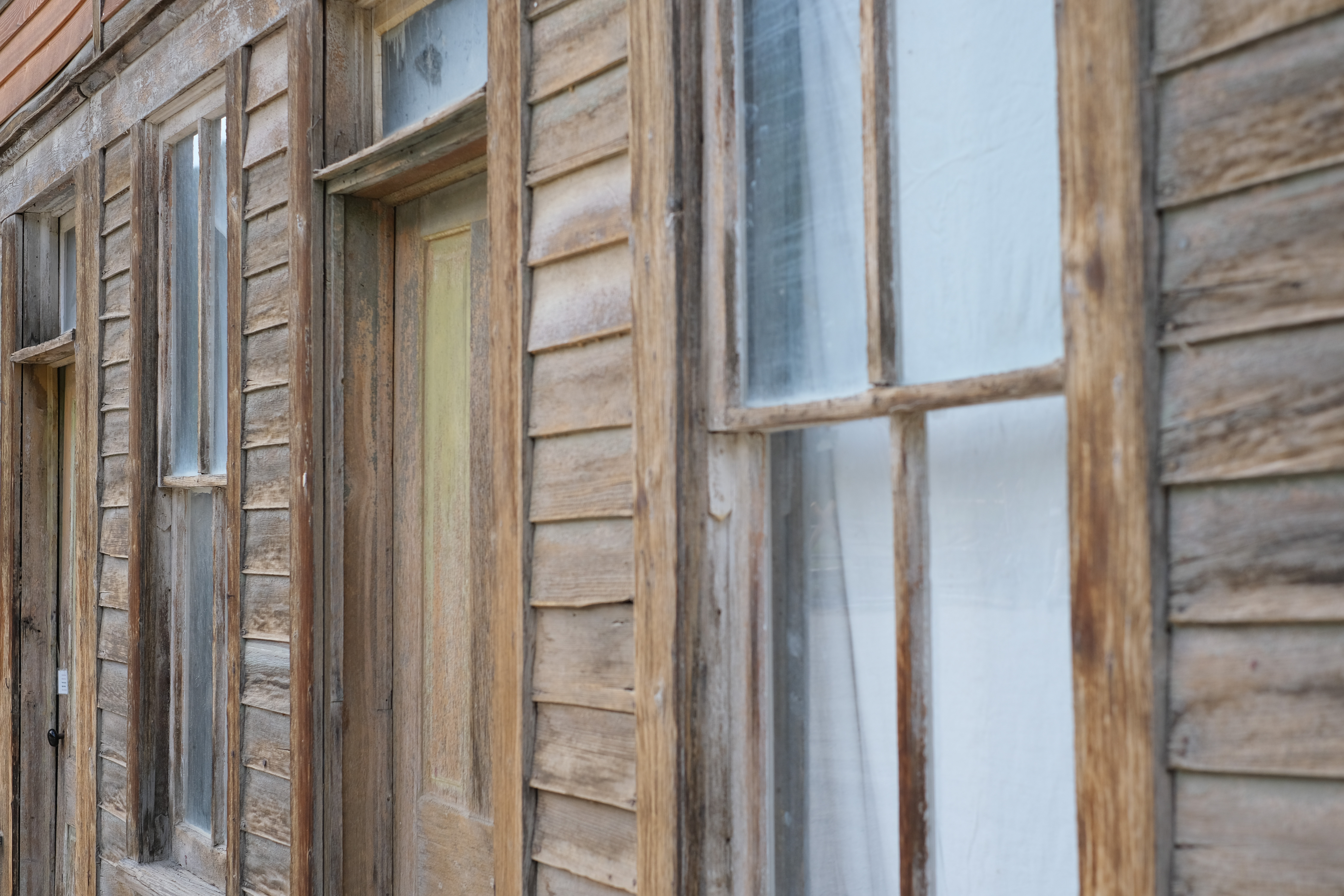 Close-up of a weathered wood-plank building exterior — clapboard siding, an old paned window, a door with peeling paint.