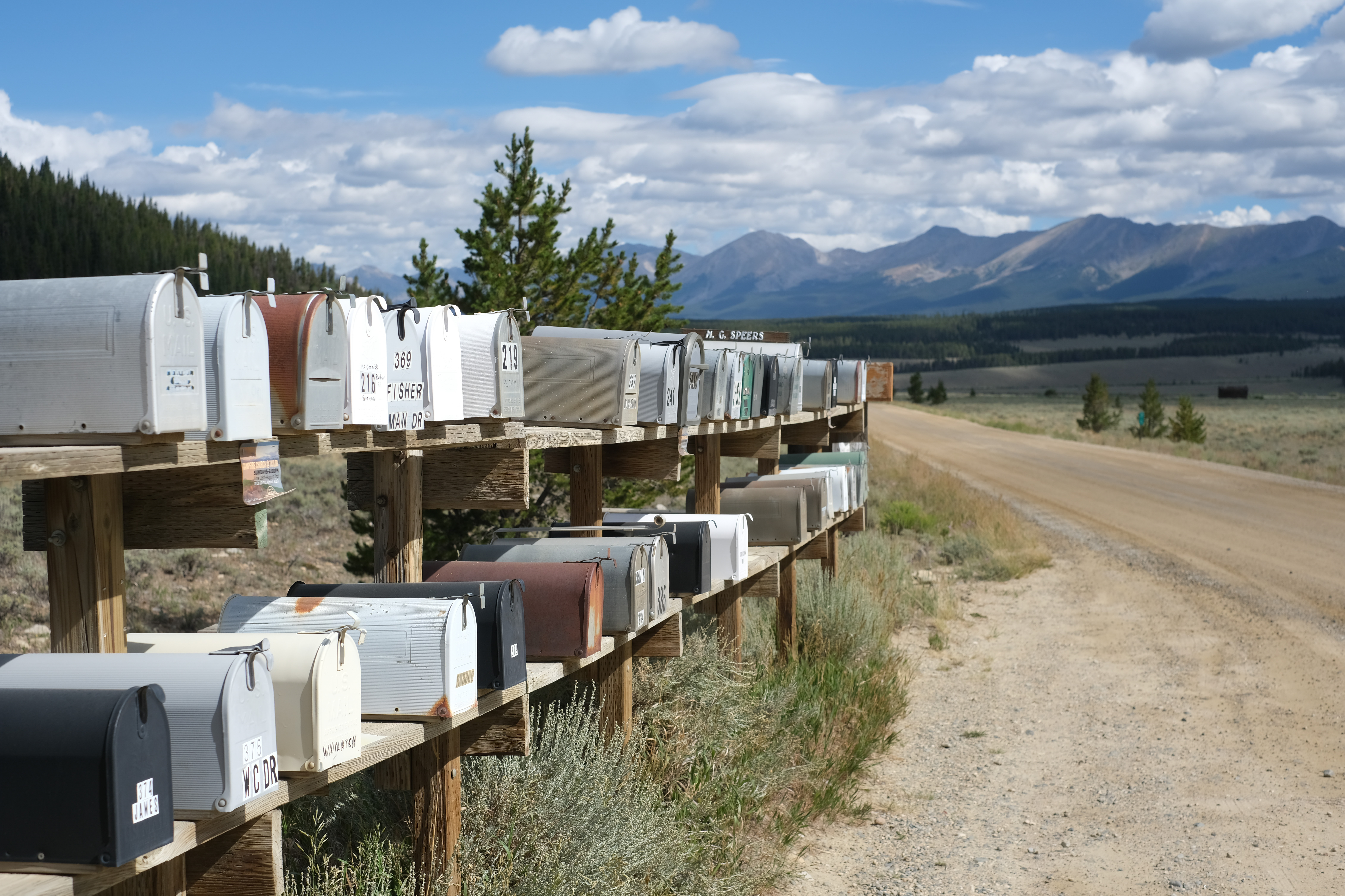 A long row of rural mailboxes along a dirt road, mountains in the distance.