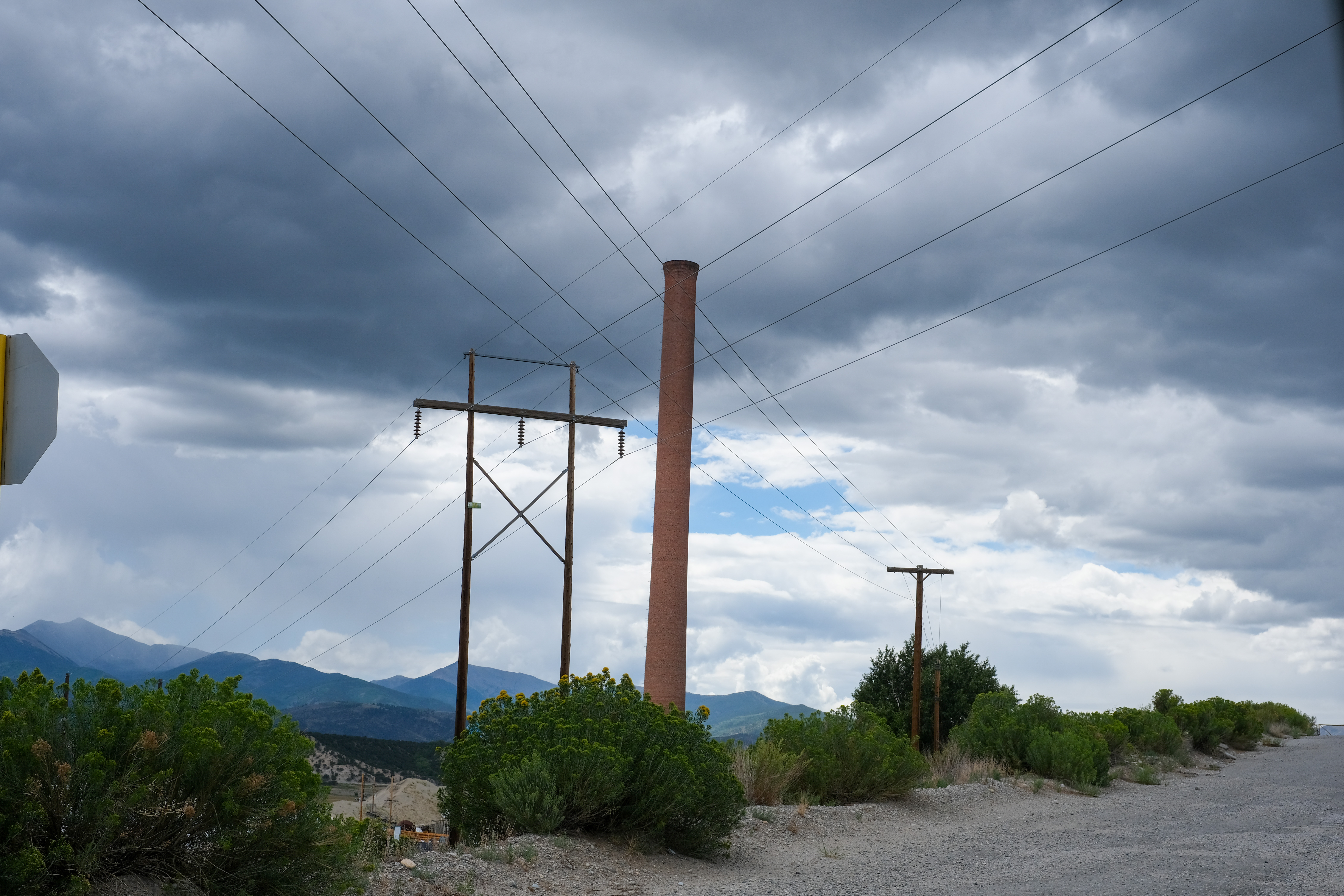 An old brick smokestack and power lines against a heavy storm sky.