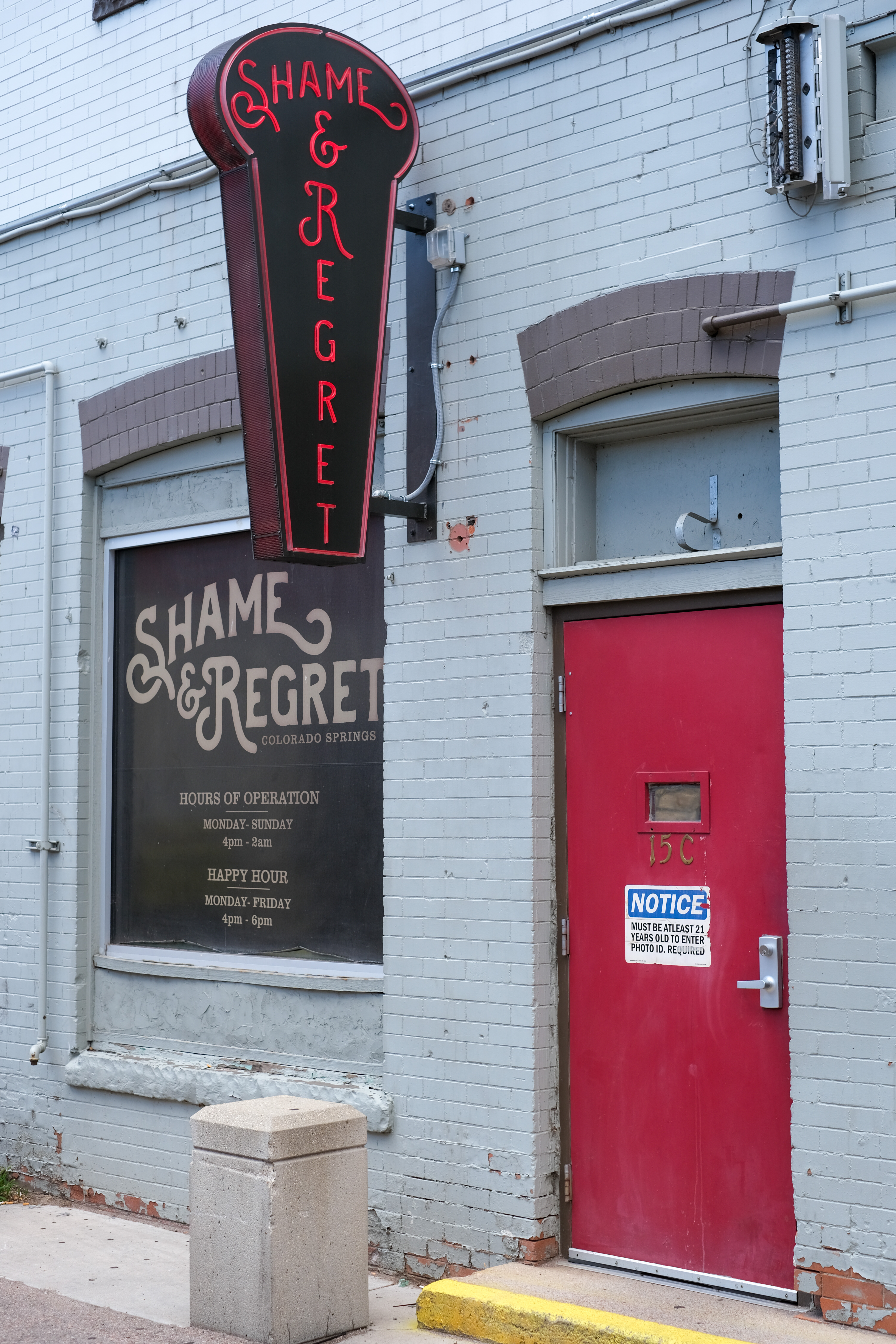 A neon "Shame & Regret" sign over a red door in downtown Colorado Springs.