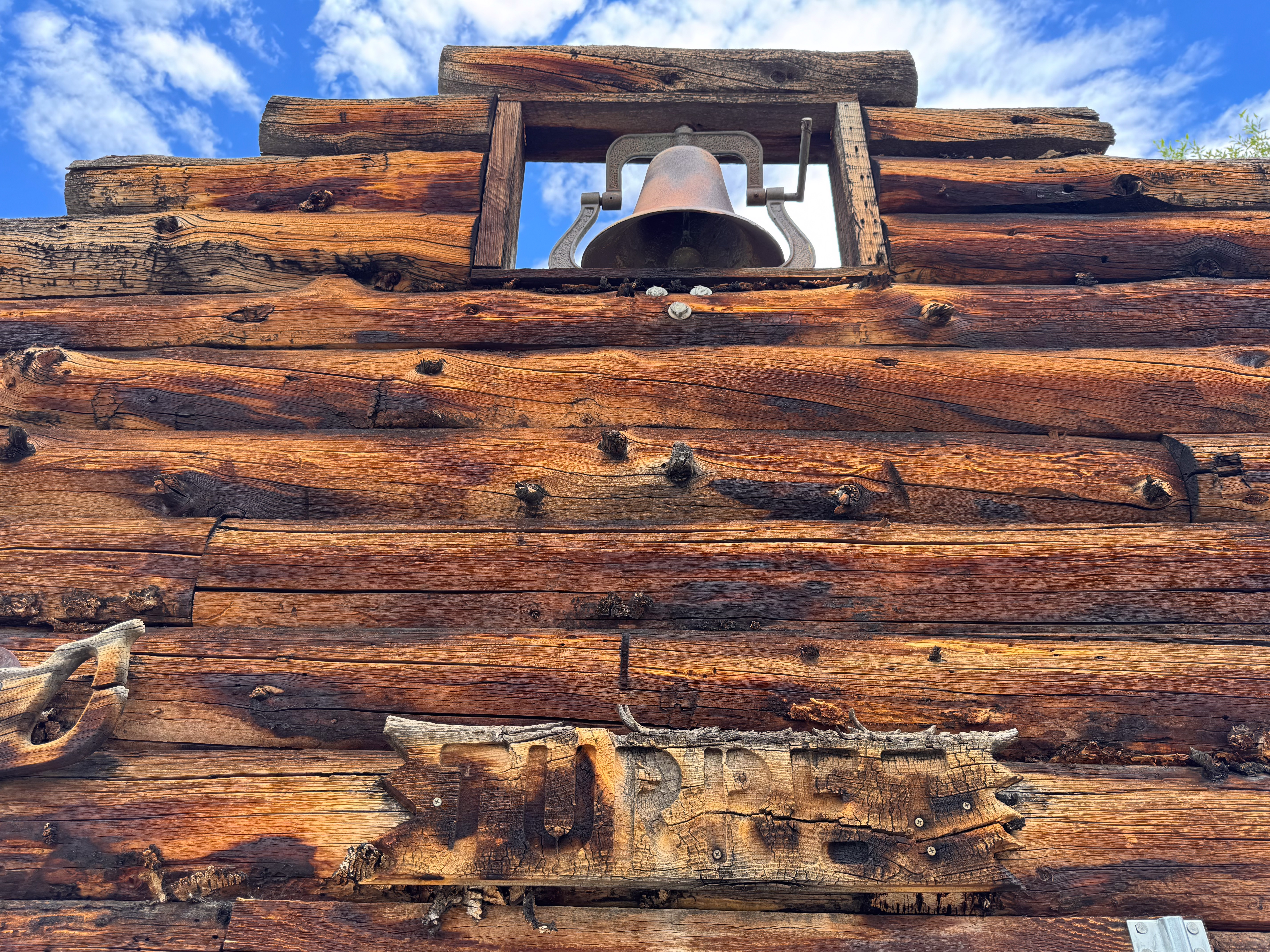 A hewn-log building in Turret — an old bell in the cupola, a carved sign reading "TURRE..."