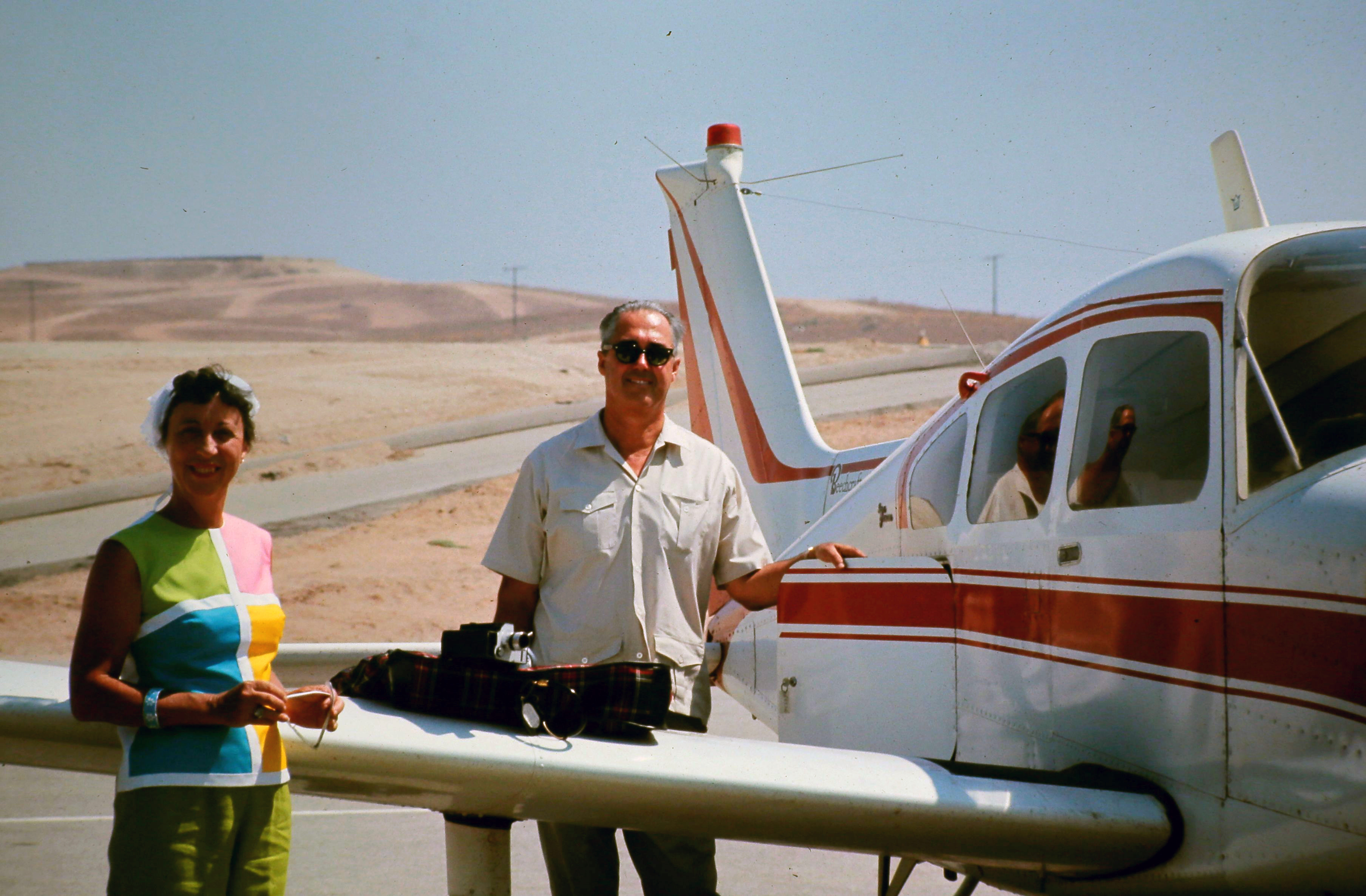 Gram beside Gramp's first Beechcraft at a desert airstrip, est. 1968–1973