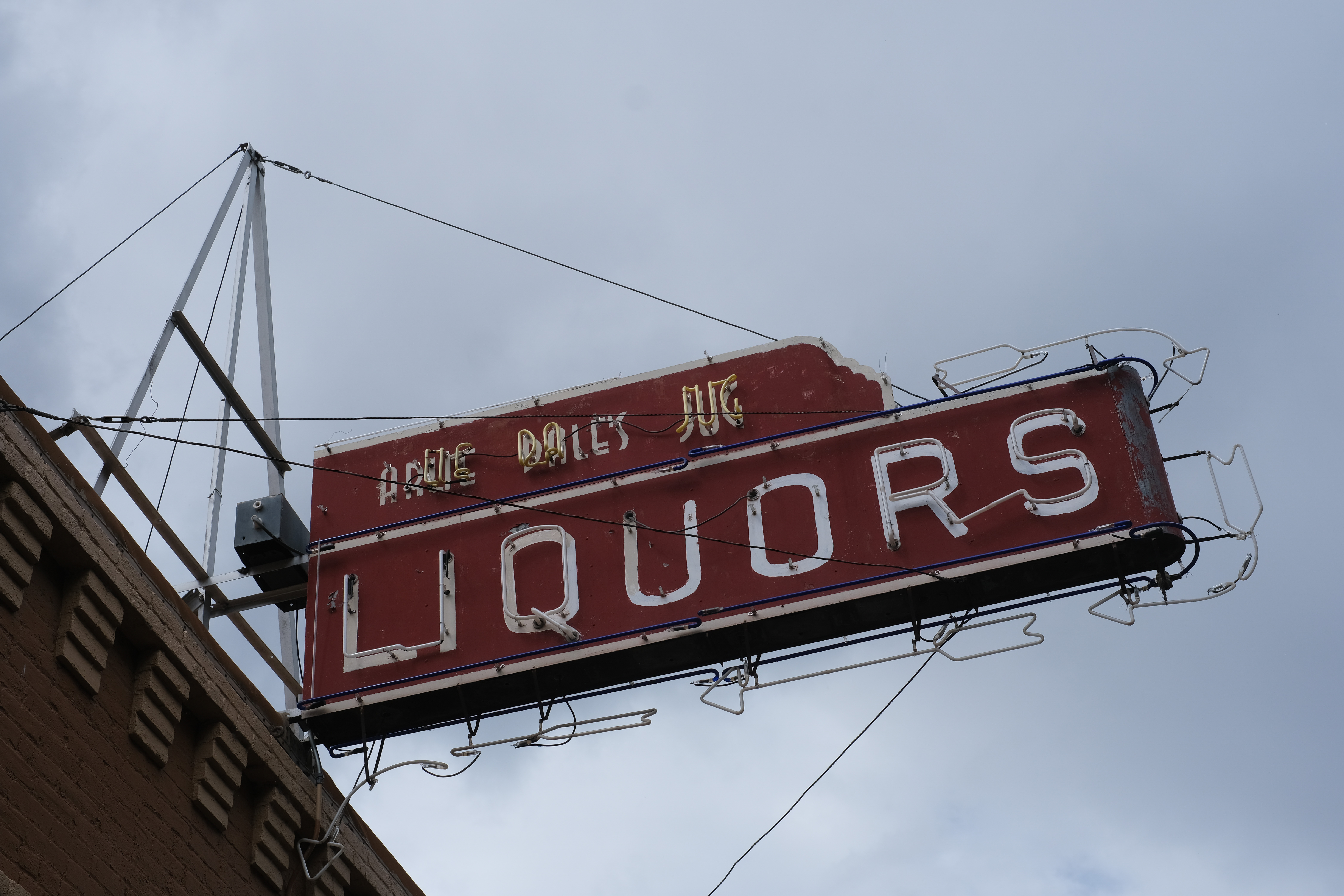 A vintage double-sided neon sign reading "Uncle Dale's Jug — Liquors" mounted above a brick building corner.