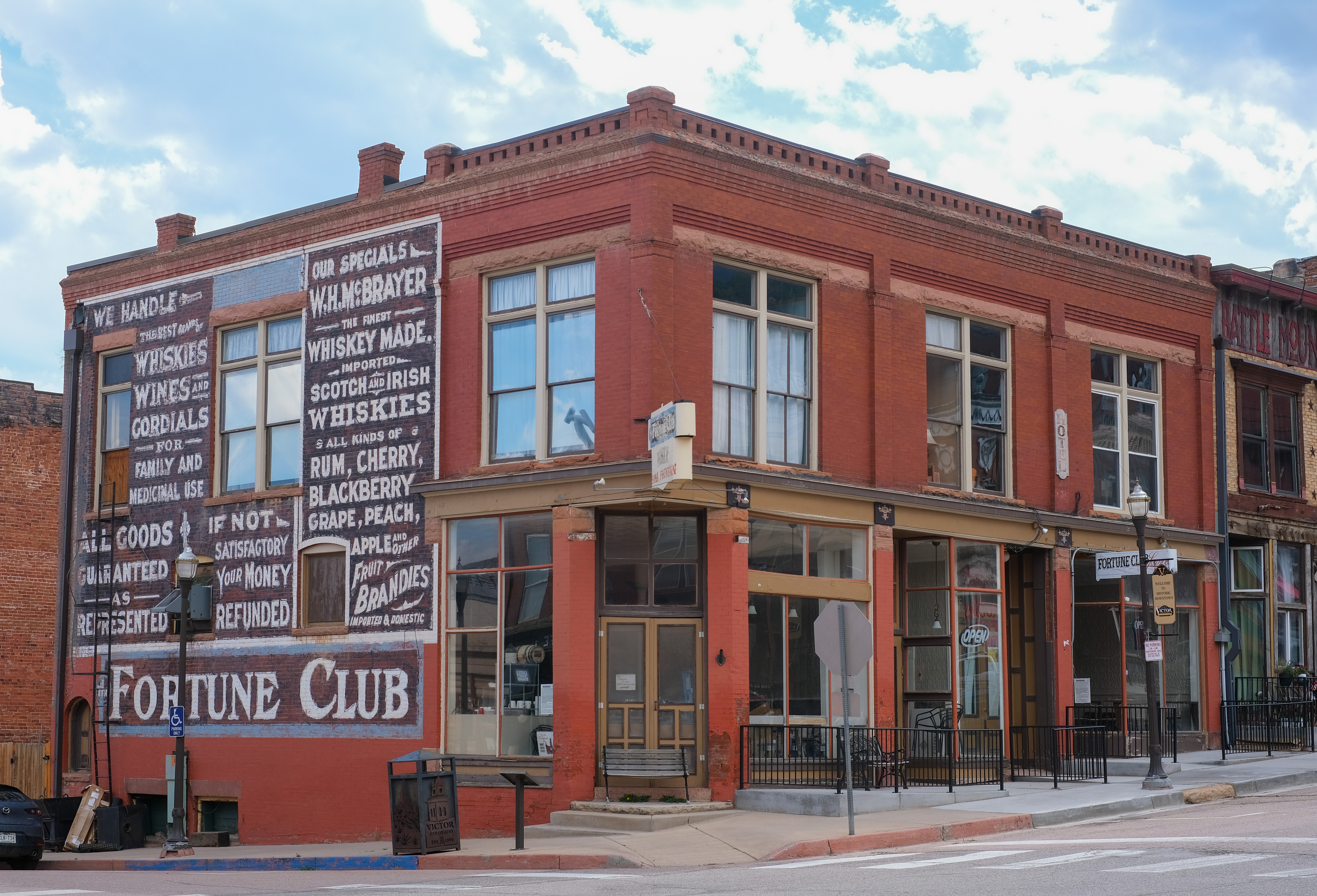 A full corner building in Victor — an upper-wall whiskey ad ghost sign, a live storefront below, and a "Victor, Colorado" plaque at the sidewalk.
