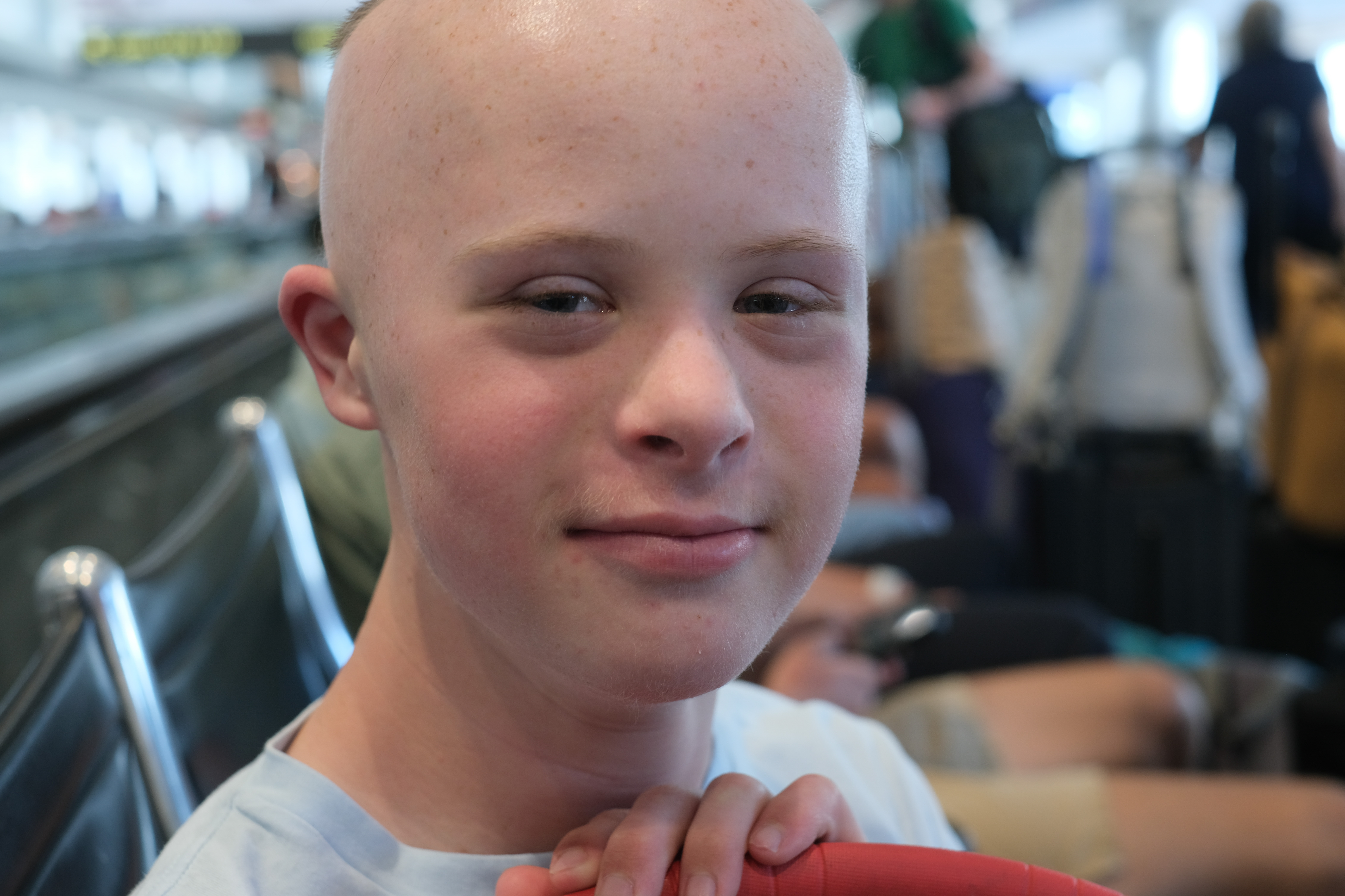 Black-and-white close-up portrait of Dylan near an airport moving walkway, travelers blurred in the background.