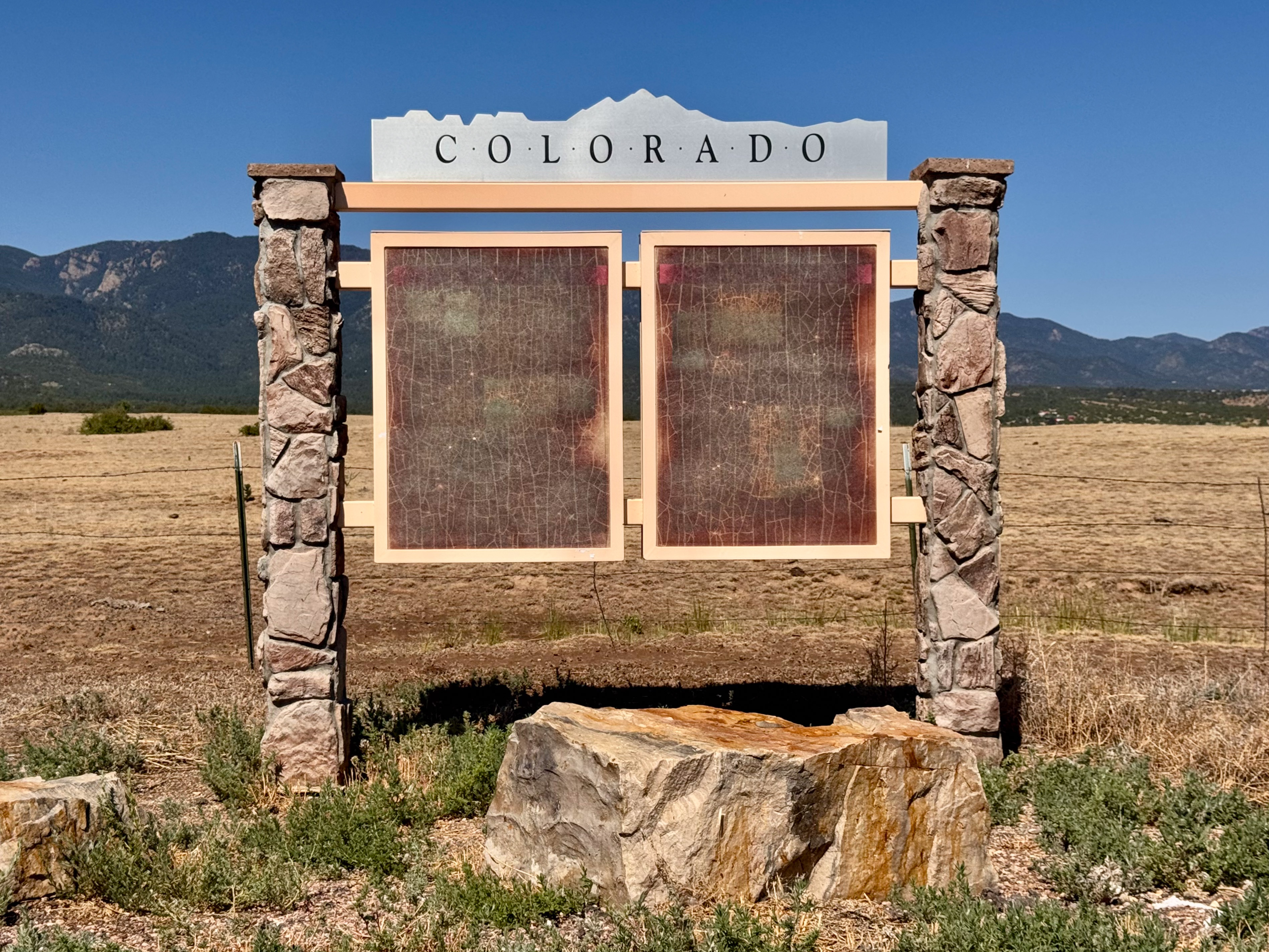 A weathered highway "Colorado" welcome sign, its plexiglass panels sun-bleached and cracked to illegibility.