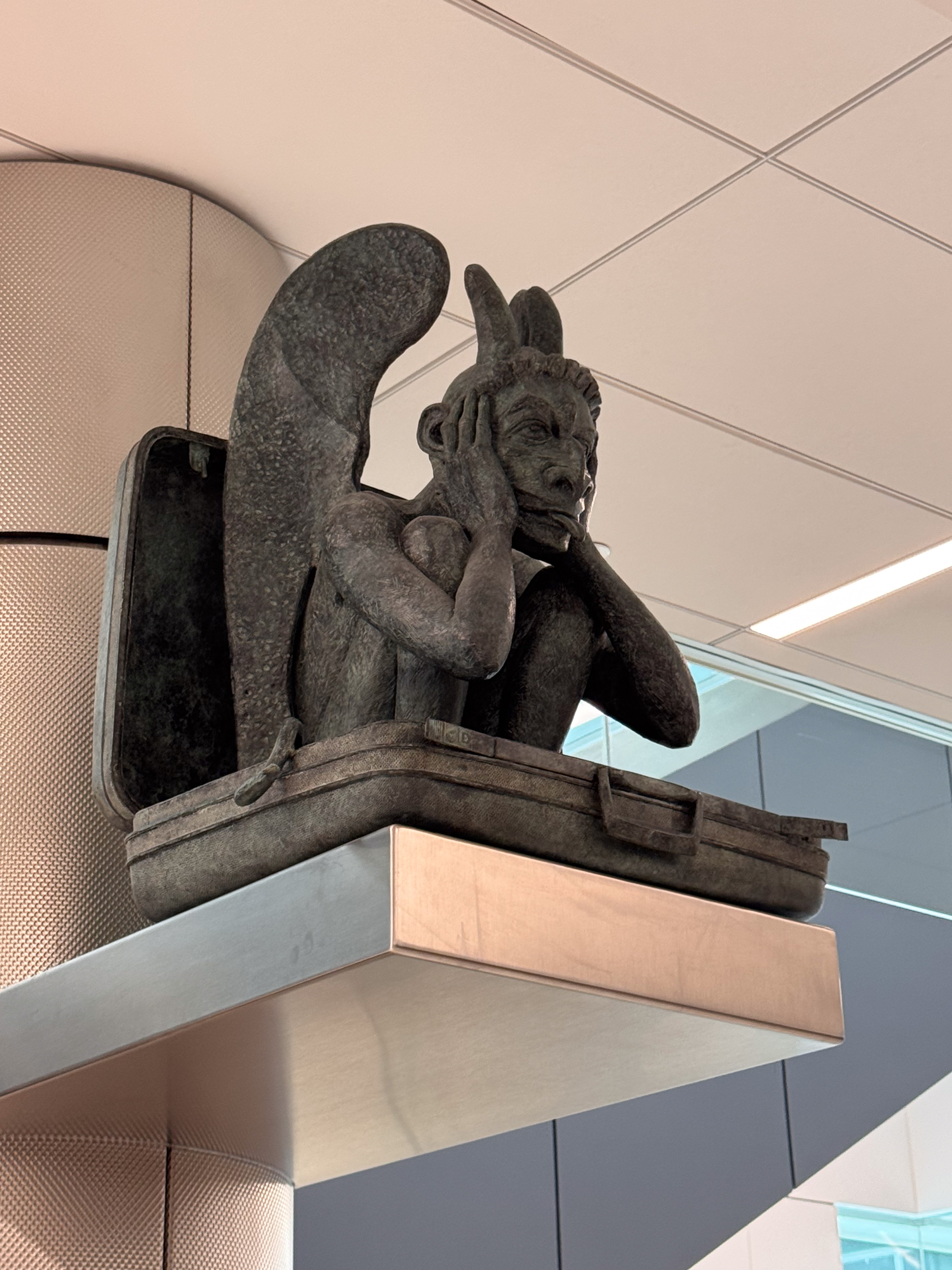 A bronze gargoyle sculpture perched on an open suitcase, overlooking the terminal at Denver International Airport.