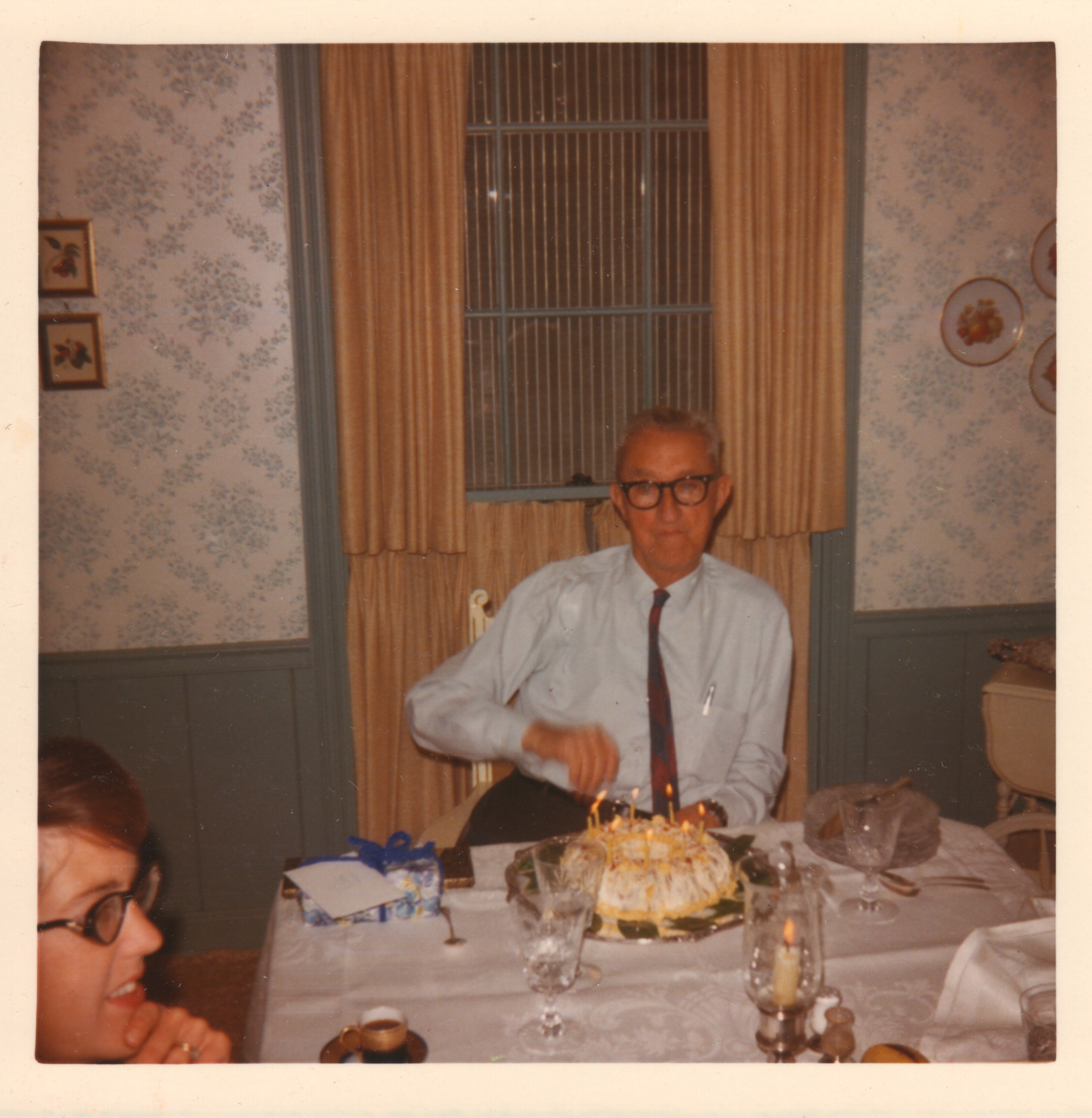 H.P. at the head of the table behind a candle-lit birthday cake. Est. 1960s.