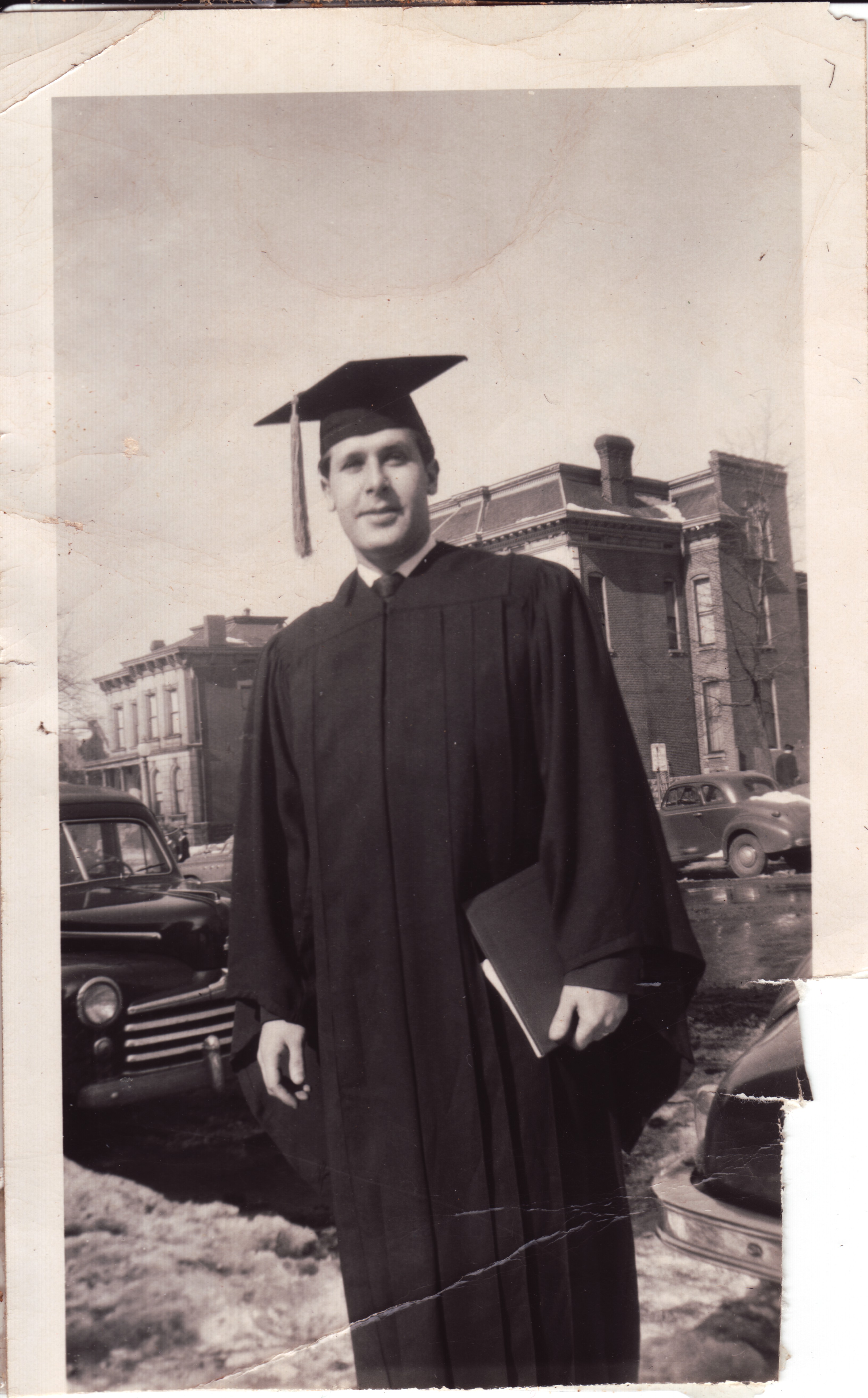 A young man in cap and gown on a St. Louis street, late 1940s — believed to be George Shulman at his graduation (filed under his name; identification not yet confirmed by family)