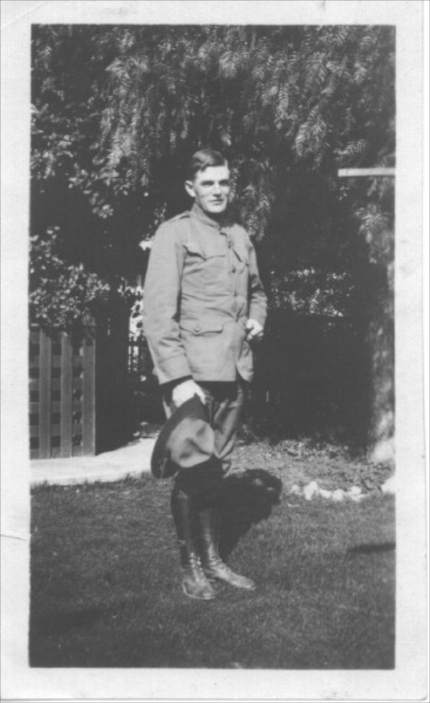 Young Elmer in his WWI Army uniform, standing in a yard holding his campaign hat, est. 1918