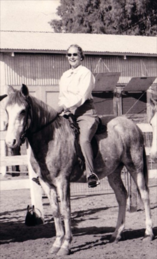 Muriel on horseback in the El Centro stable yard, grinning behind sunglasses. Est. 1965–1975.